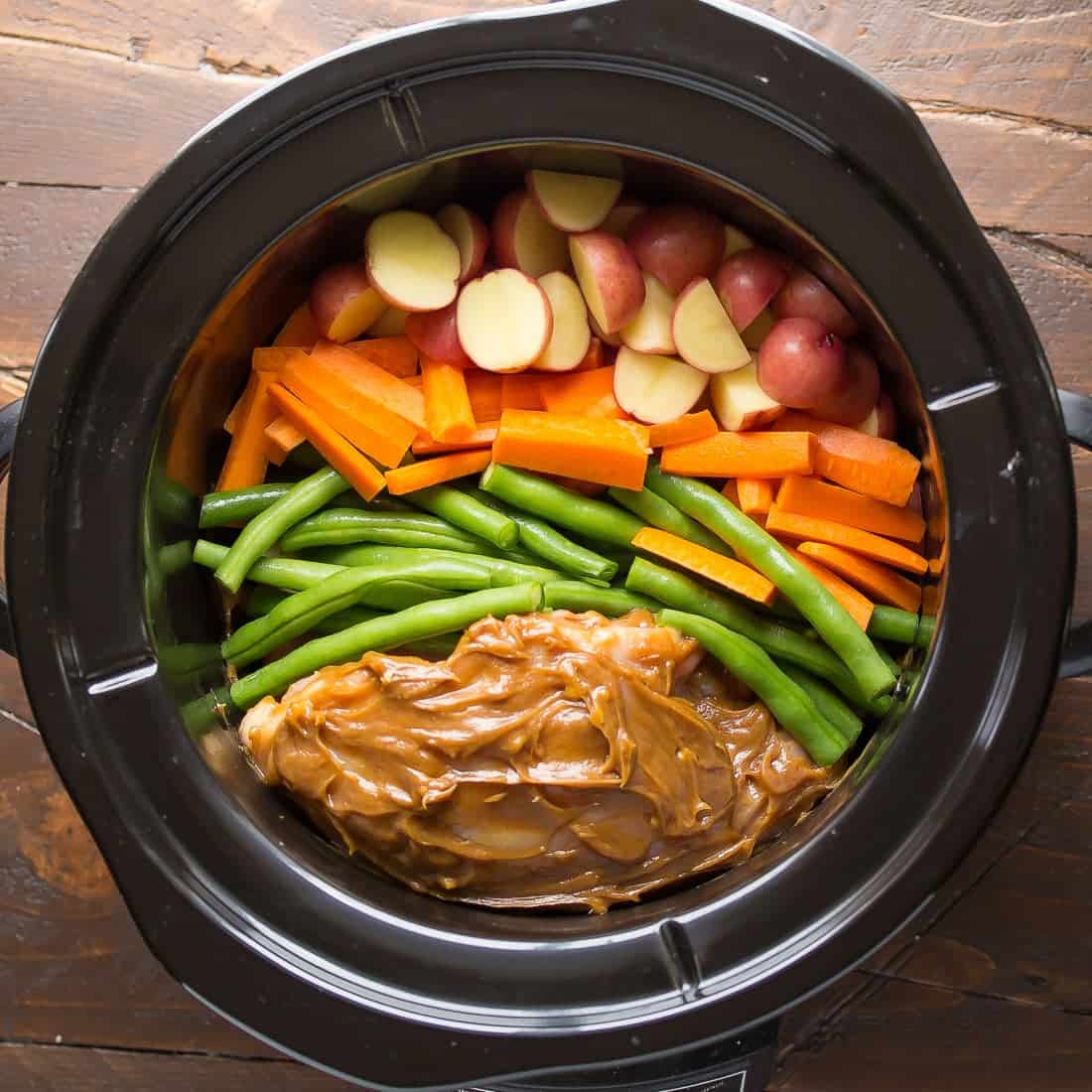overhead view of Thai peanut chicken in slow cooker with carrots, beans and potatoes before cooking