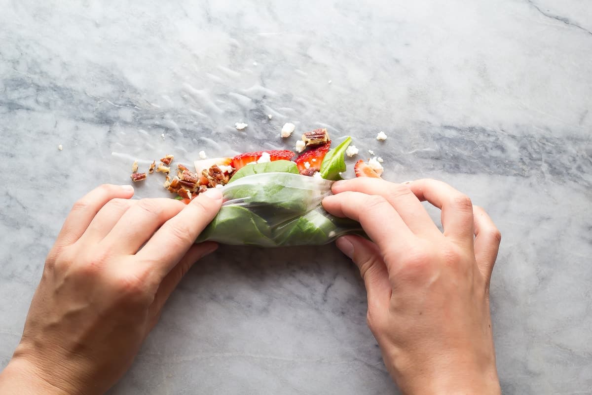 hands rolling a strawberry spinach spring roll