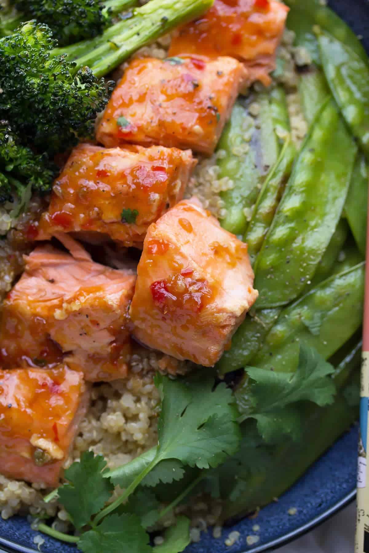 A delicious and healthy dinner recipe: sweet chili salmon is served with roasted broccoli and snap peas on a quinoa bowl! Makes a great lunch, as well.
