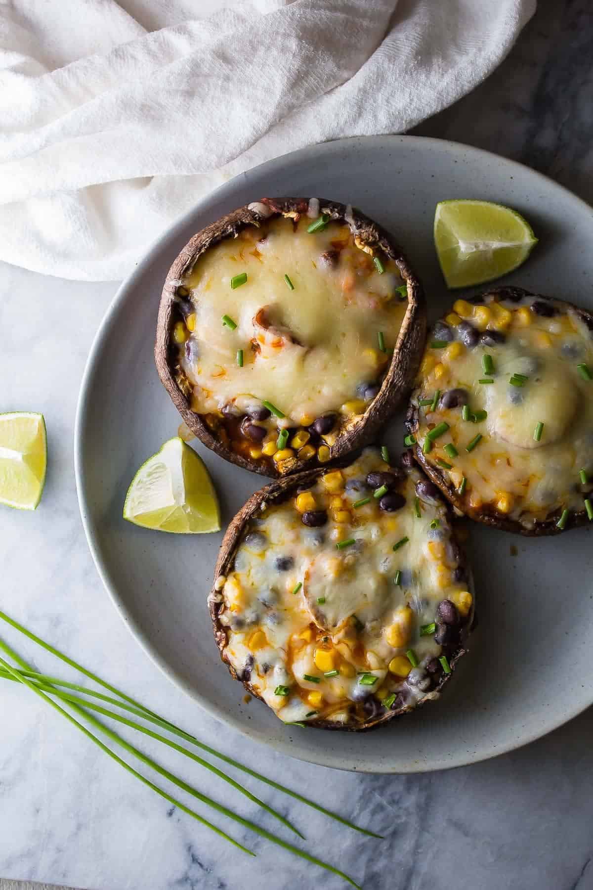 Three Enchilada Stuffed Grilled Portobello Mushrooms plated with chives and lime slices