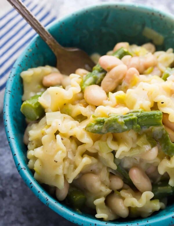 pasta with asparagus leeks and white beans in blue bowl with a fork