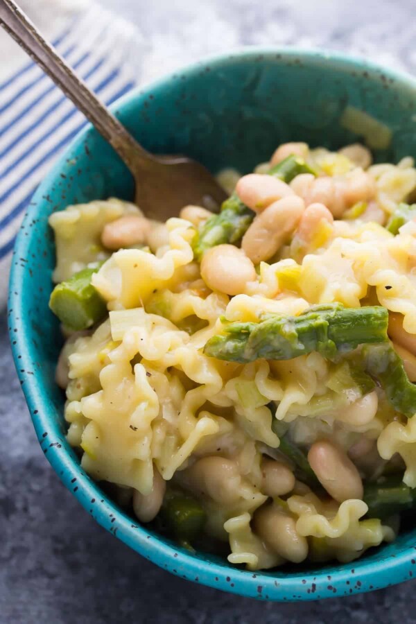 pasta with asparagus leeks and white beans in blue bowl with a fork