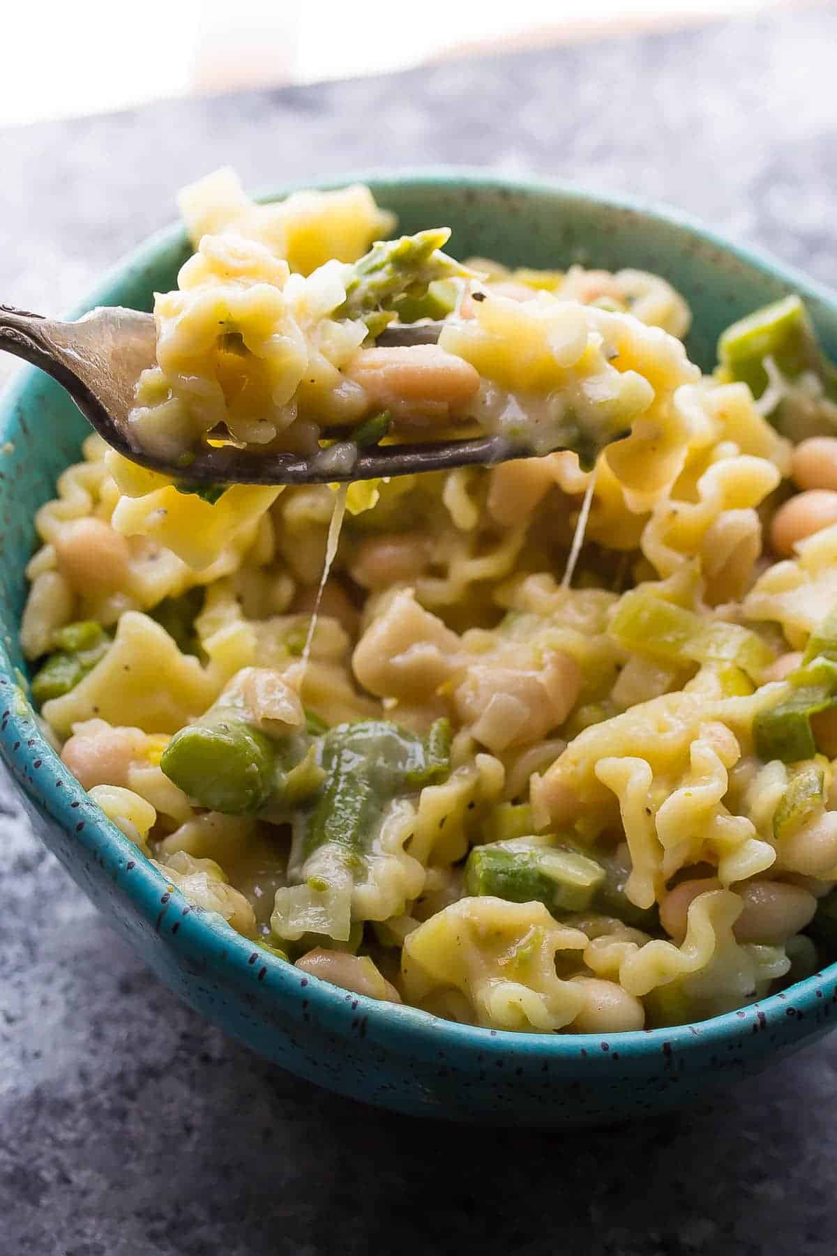 fork digging into a bowl of pasta with leeks and white beans