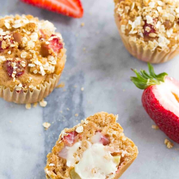 three strawberry apple crumble muffins on gray counter with fresh strawberries