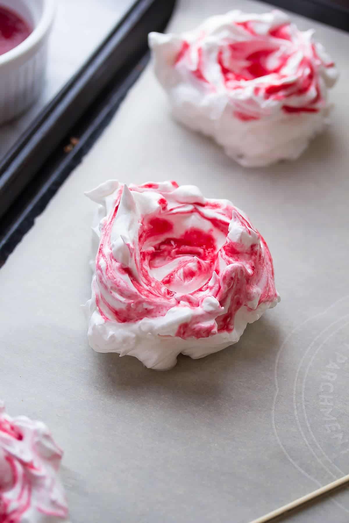 swirled raspberry meringue nests on baking sheet before baking through