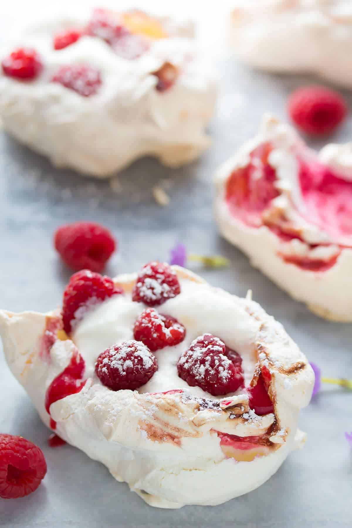 side view of raspberry meringue nests topped with whipped cream, fresh berries and powdered sugar