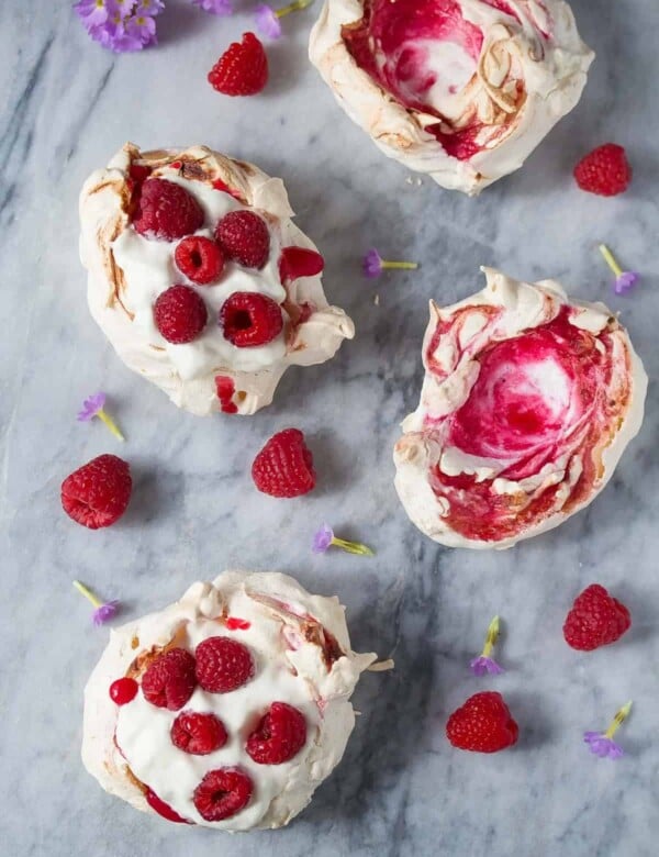 overhead shot of four raspberry swirl meringue nests and fresh raspberries on gray counter