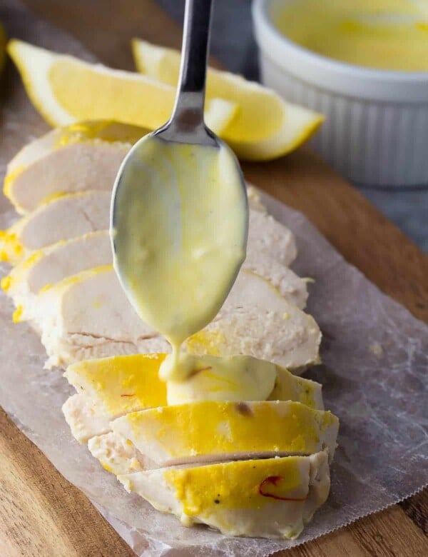 saffron garlic yogurt chicken sliced on parchment with spoon drizzling dressing