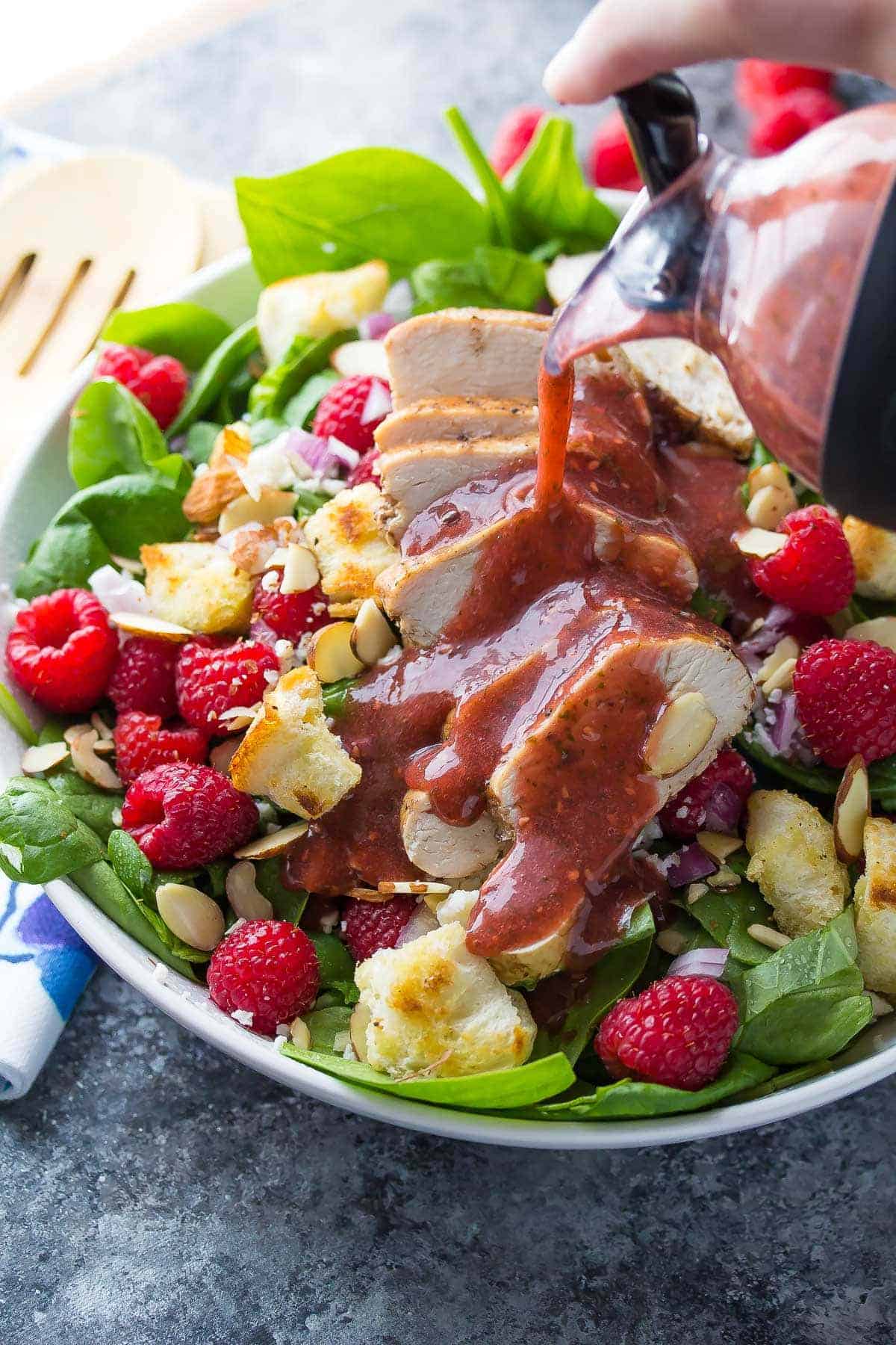 Full bowl of Raspberry Spinach Panzanella Salad with Chicken and Raspberry Basil Vinaigrette poured on top 