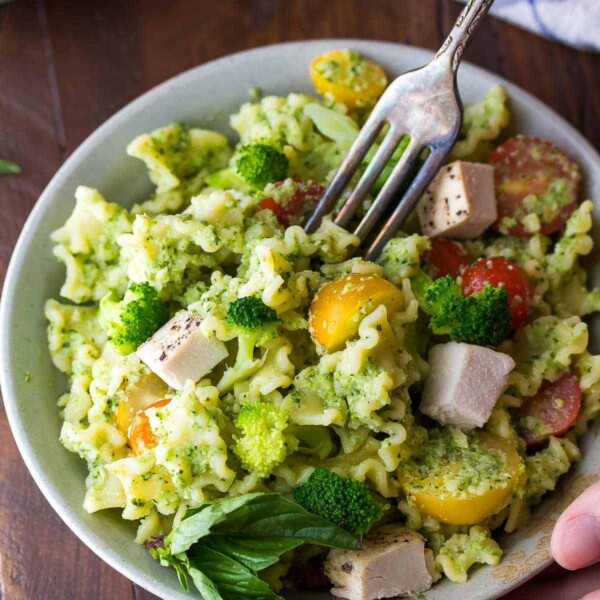 almond broccoli pesto pasta in white bowl with a fork taking a bite