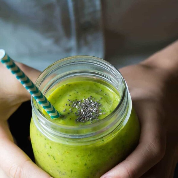 hands holding a green mango superfood smoothie in mason jar