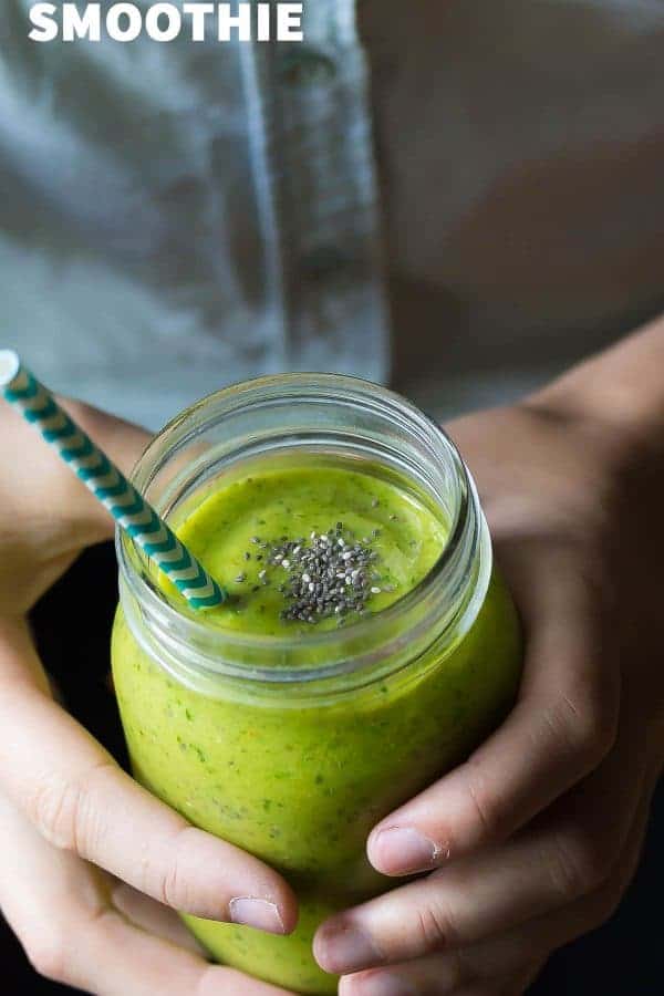 hands holding a green mango superfood smoothie in mason jar