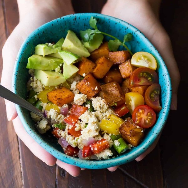 hands holding a blue bowl with tofu breakfast scramble with sweet potatoes and avocado