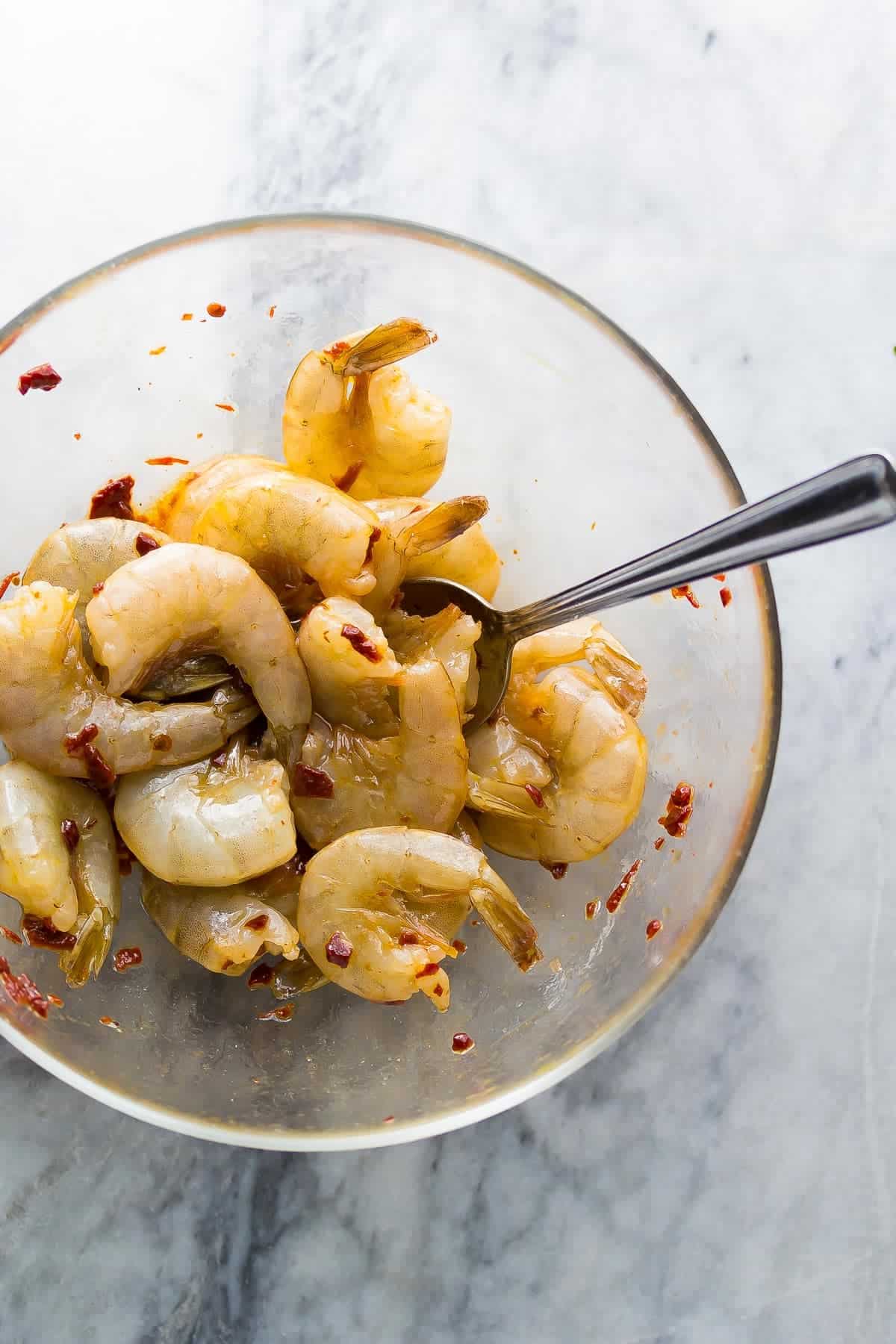 Raw shrimp in a bowl being seasoned with marinade