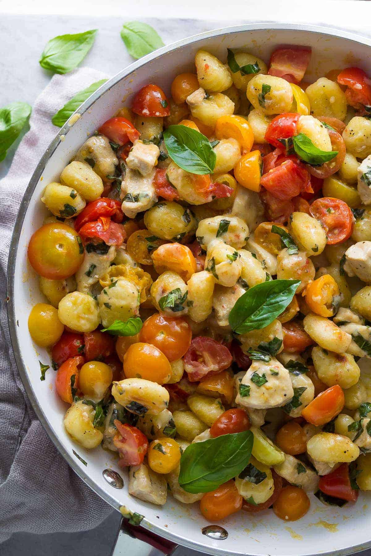 Summery Caprese Chicken Gnocchi in a skillet decorated with basil