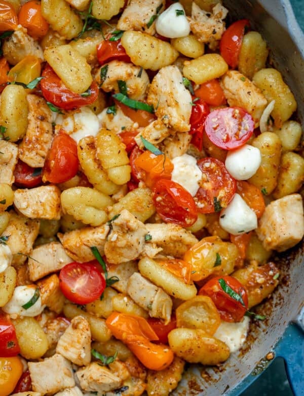 an overhead shot of chicken, gnocchi and tomatoes in a skillet