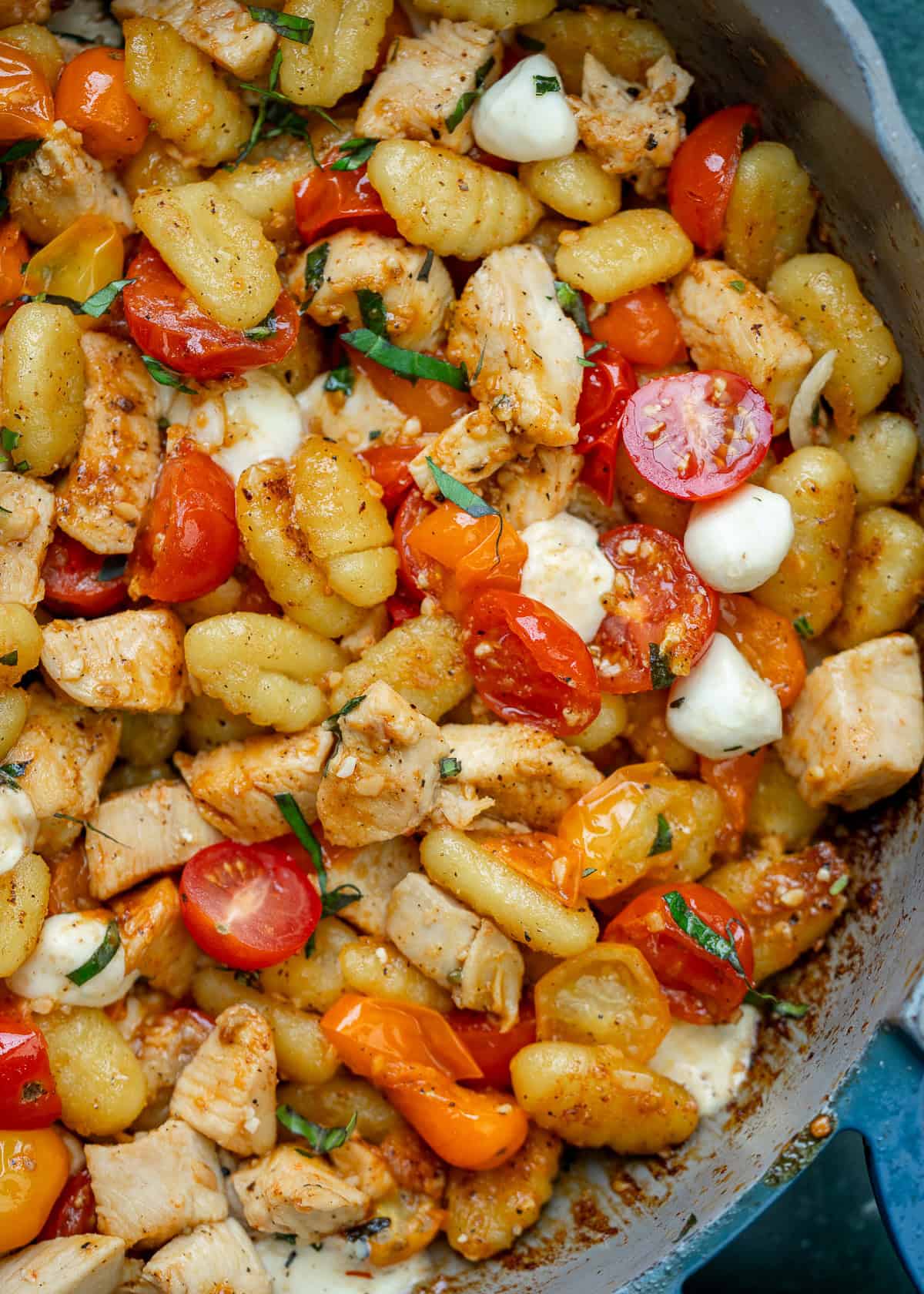 an overhead shot of chicken, gnocchi and tomatoes in a skillet