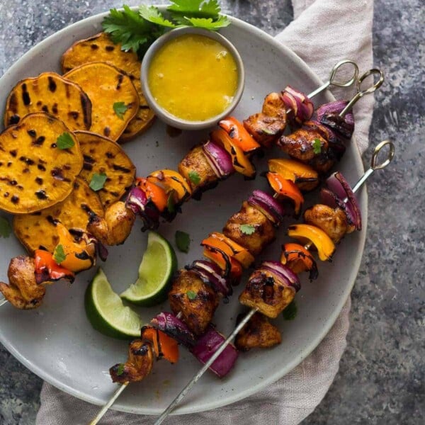 three chili rubbed chicken skewers with mango dipping sauce and sweet potato chips on gray plate