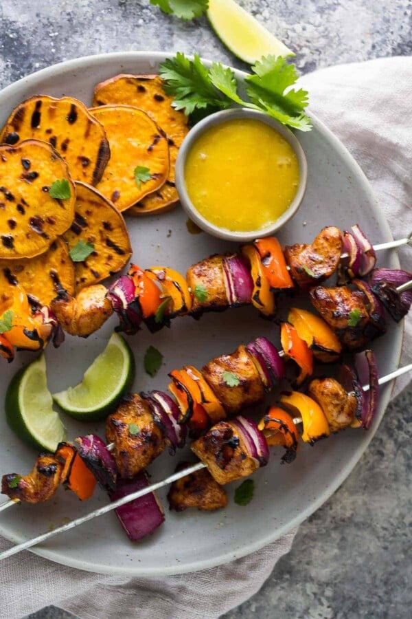 three chili rubbed chicken skewers with mango dipping sauce and sweet potato chips on gray plate