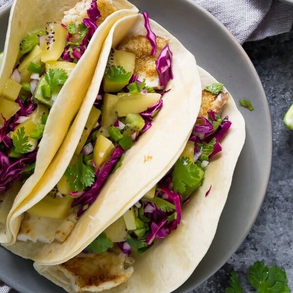 three grilled fish tacos with jalapeno kiwi salsa and cilantro and lime on gray plate