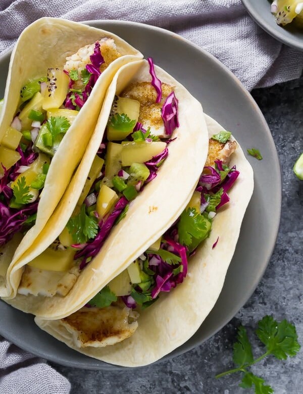 three grilled fish tacos with jalapeno kiwi salsa and cilantro and lime on gray plate