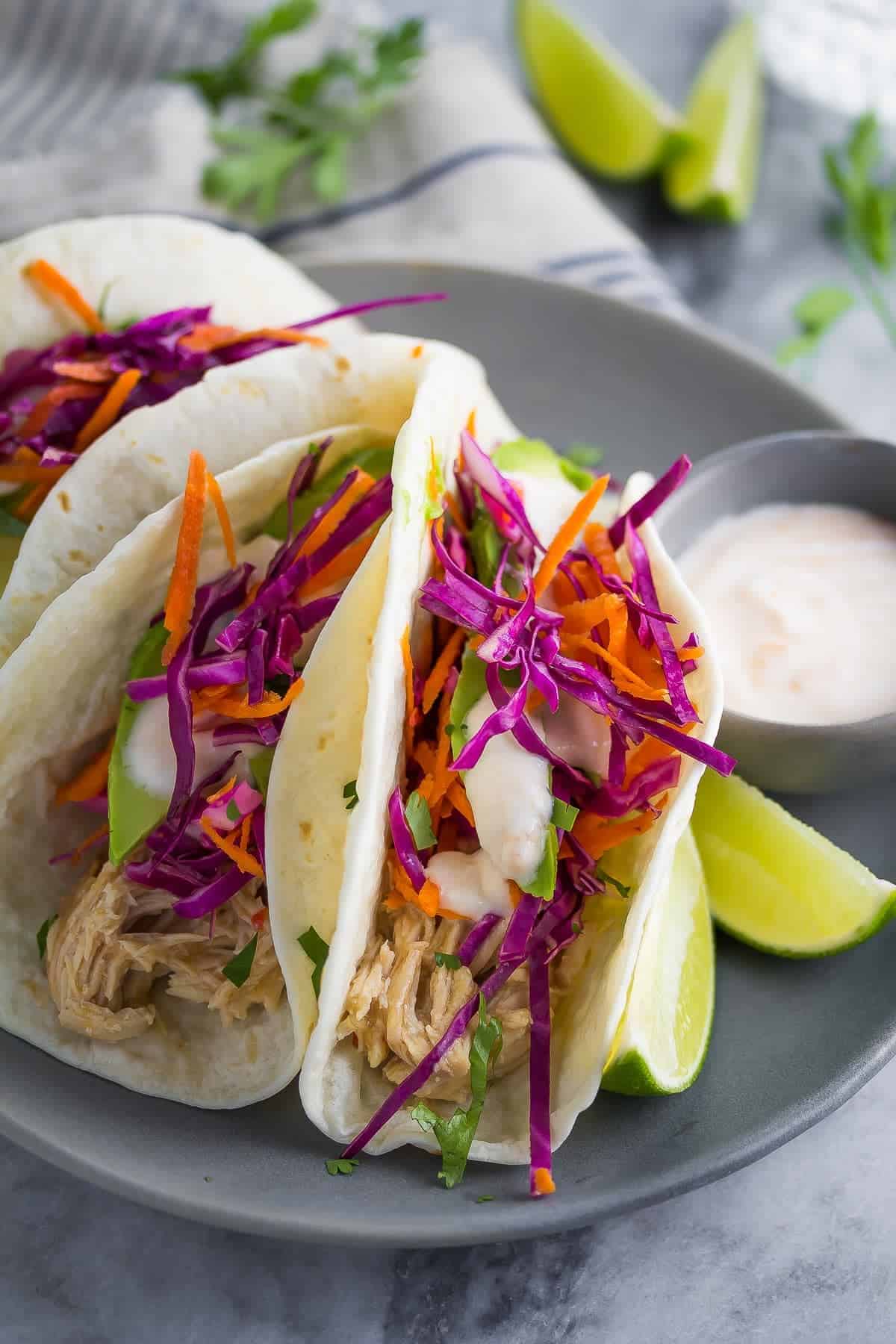 side angle view of Sweet Chili Chicken Tacos plated with slaw and yogurt sauce