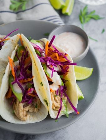 three sweet chili chicken tacos on gray plate with dipping sauce and lime wedges