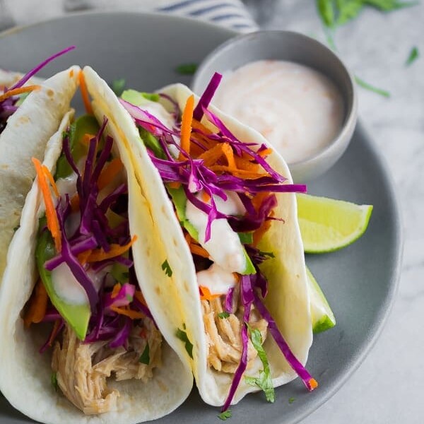 three sweet chili chicken tacos on gray plate with dipping sauce and lime wedges