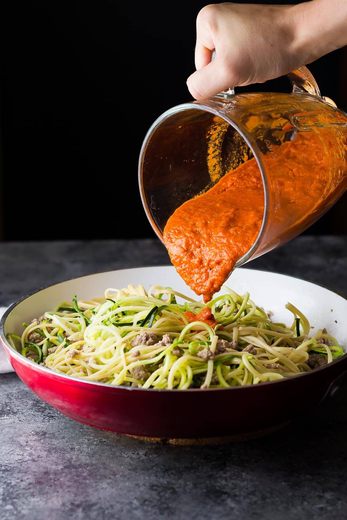 pouring romesco sauce over ground turkey pasta