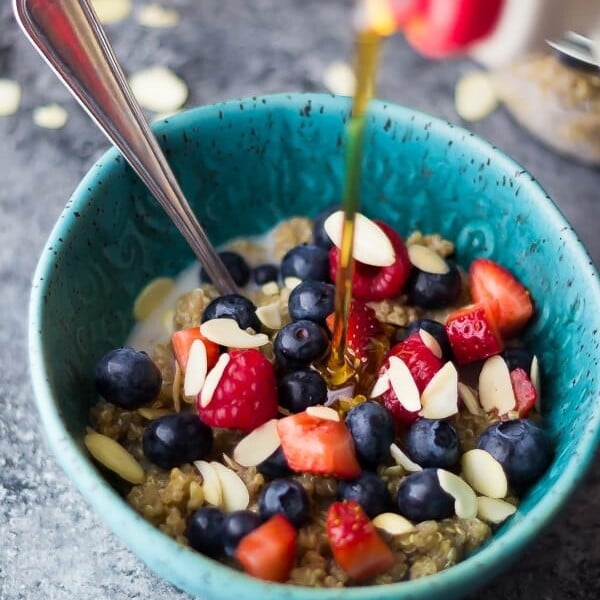 blue bowl with berry almond breakfast quinoa and syrup being drizzled onto it