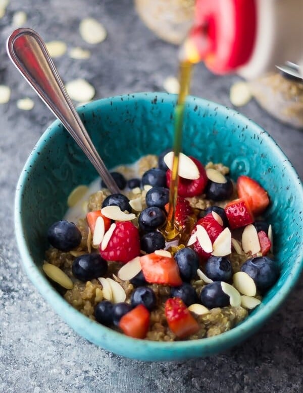 blue bowl with berry almond breakfast quinoa and syrup being drizzled onto it