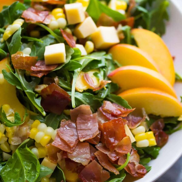 peach corn arugula salad in large white bowl