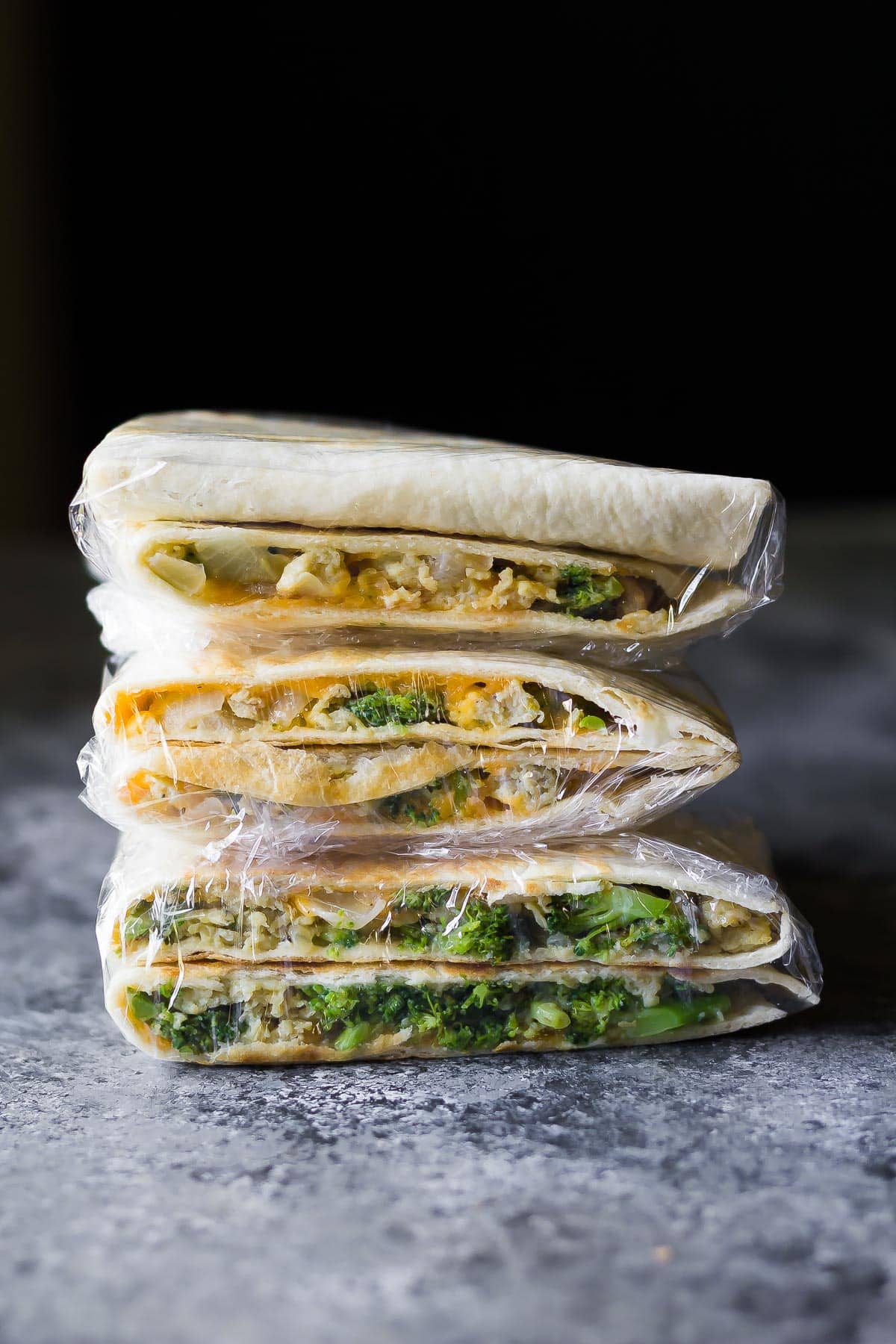 stack of Broccoli Cheddar Breakfast Quesadillas wrapped in plastic, ready for the freezer