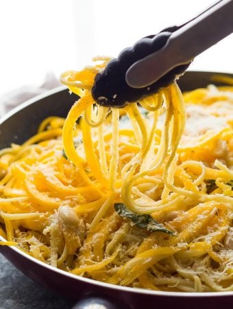 Close up shot of tongs taking out butternut squash noodles from large bowl
