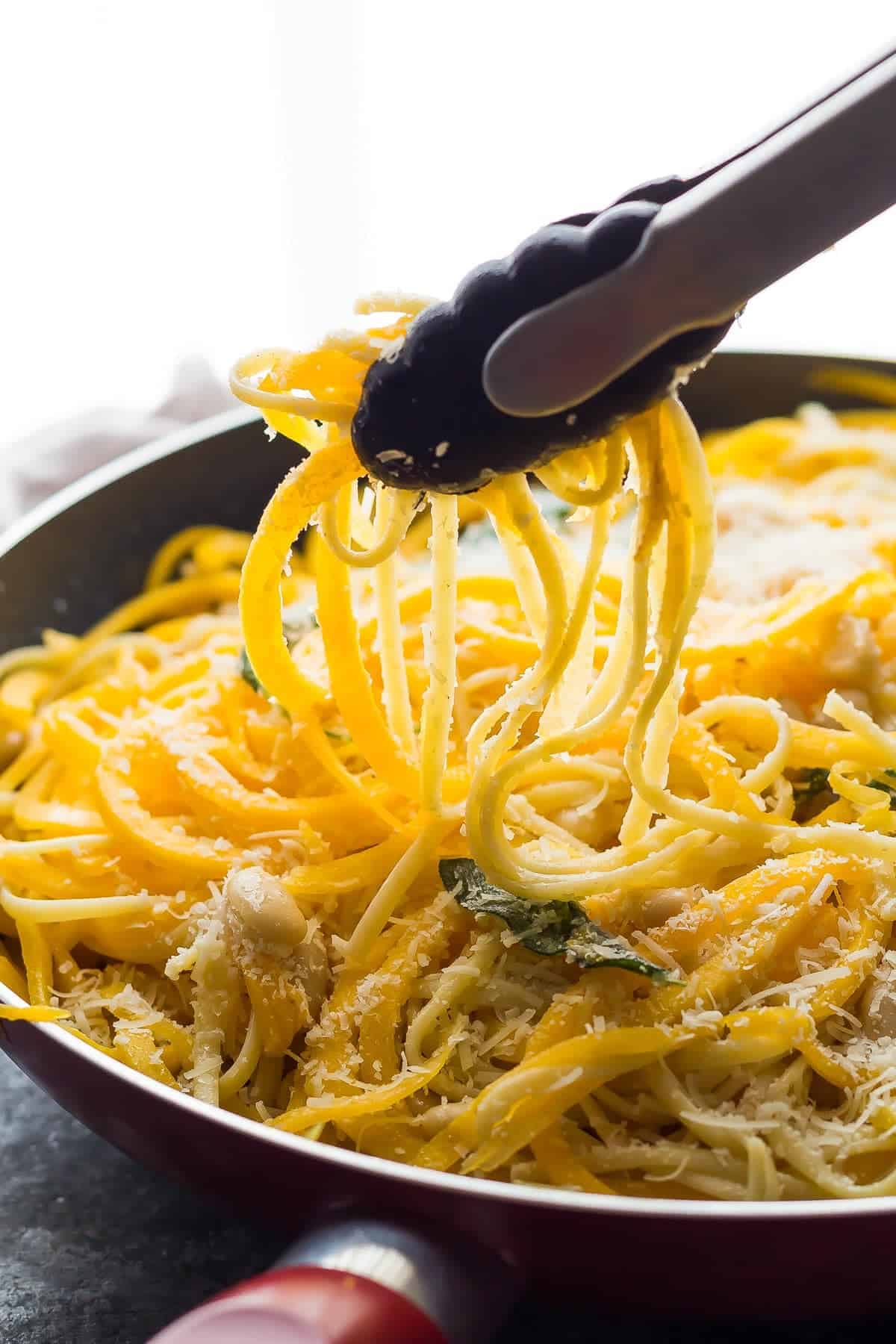 tongs lifting butternut squash noodles out of a pan