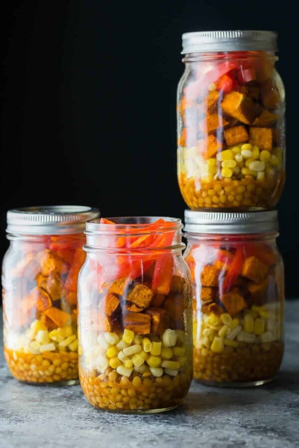 four mason jars filled with southwestern lentil sweet potato lunch bowls