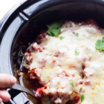 hand scooping spoonful of mexican chicken thighs out of the slow cooker