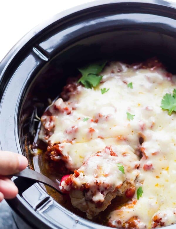 hand scooping spoonful of mexican chicken thighs out of the slow cooker