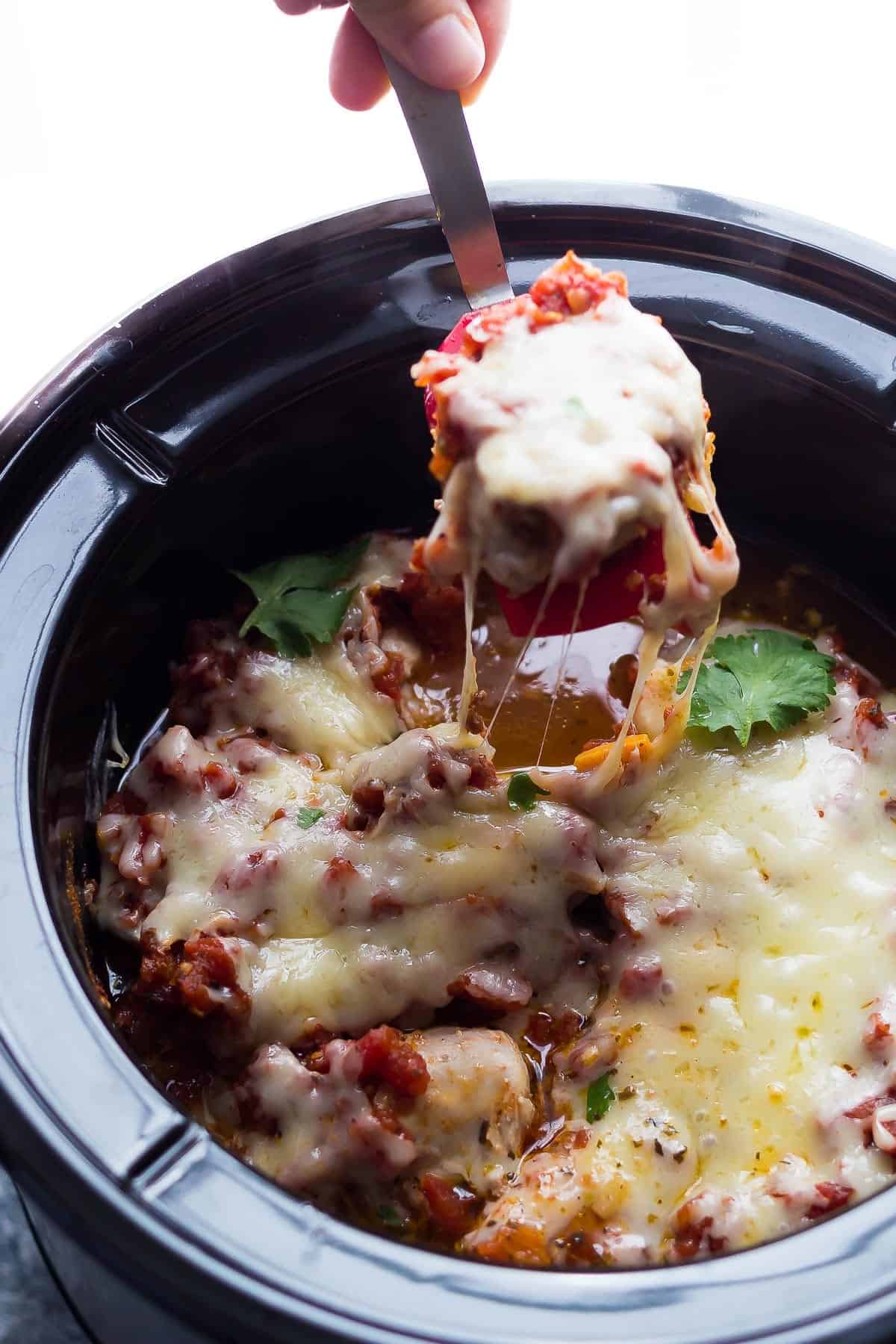 spatula lifting crockpot chicken thigh out of the slow cooker with gooey cheese