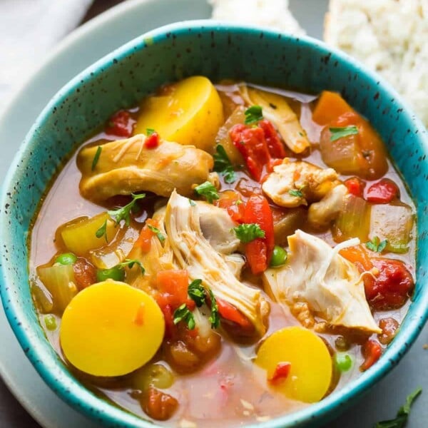 spanish chicken stew in blue bowl with piece of bread next to it