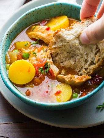hand dipping bread into the spanish chicken stew in blue bowl