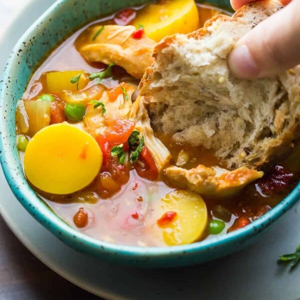 hand dipping bread into the spanish chicken stew in blue bowl