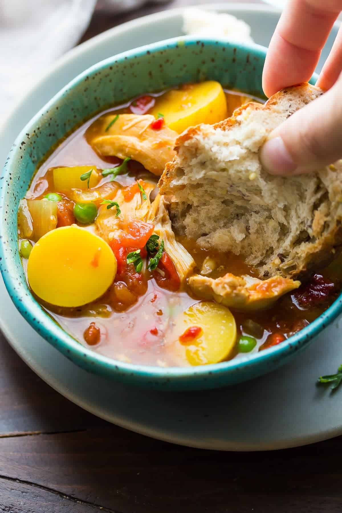 dunking bread in a bowl of Slow Cooker Spanish Chicken Stew