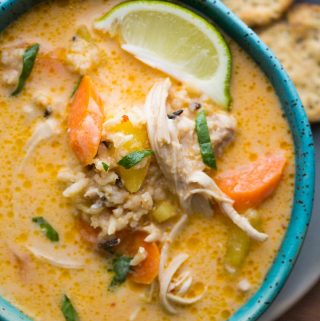 close up shot of thai slow cooker chicken and while rice soup in blue bowl with lime wedge
