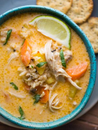 close up shot of thai slow cooker chicken and while rice soup in blue bowl with lime wedge