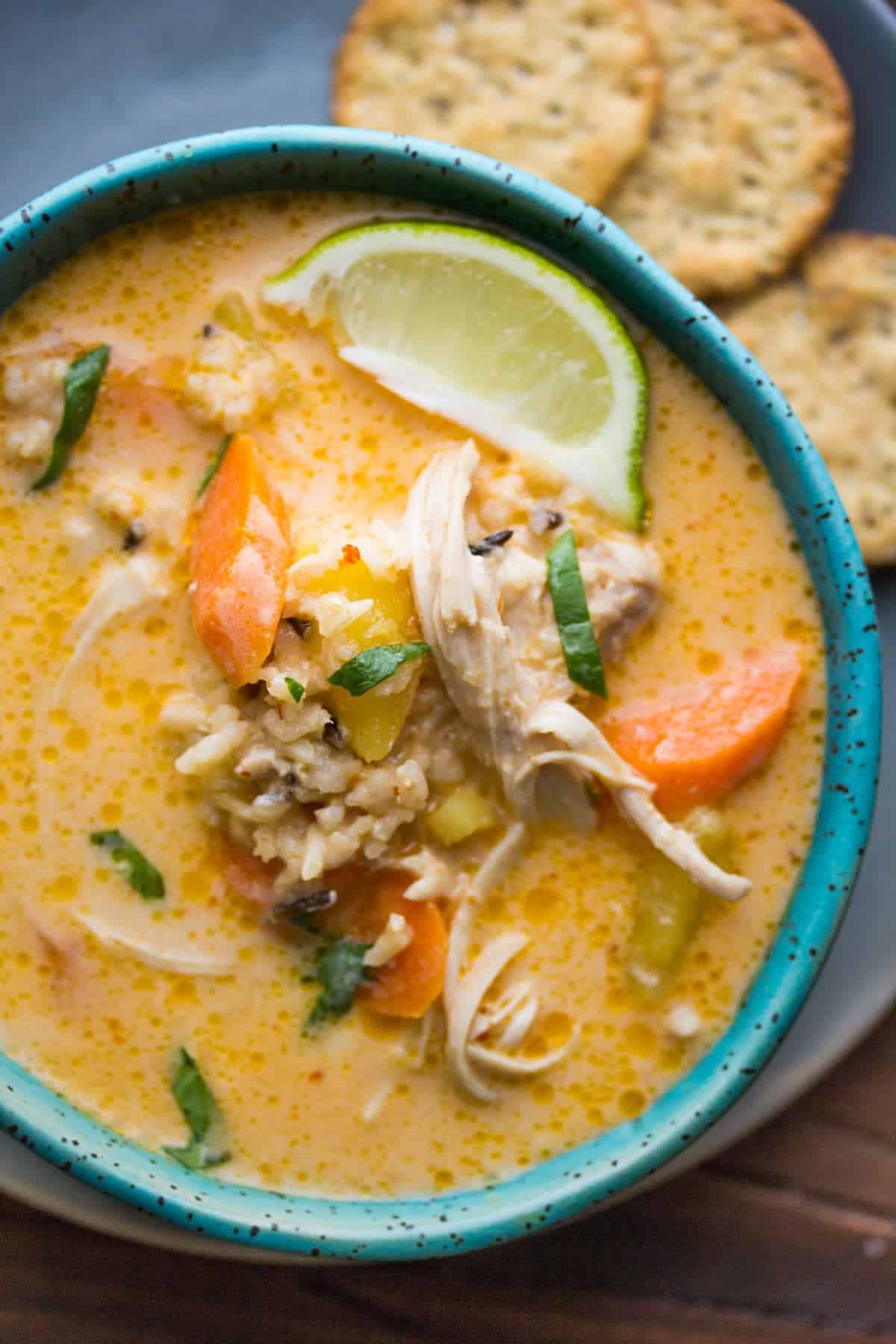 overhead close up view of thai slow cooker chicken and wild rice soup in a bowl with lime wedges