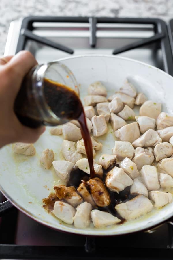 pouring stir fry sauce onto chicken in frying pan