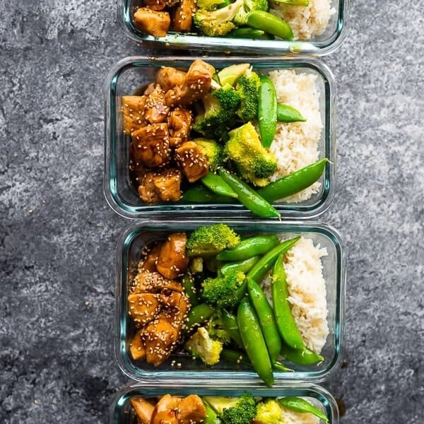 overhead shot of four meal prep containers filled with honey sesame chicken meal prep bowls