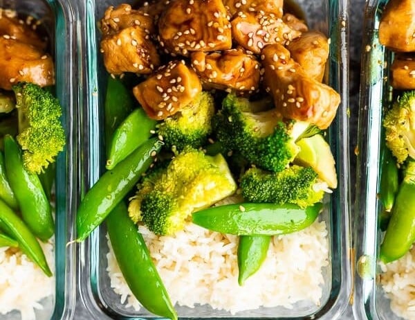 overhead shot of glass meal prep containers filled with honey sesame chicken lunch bowls