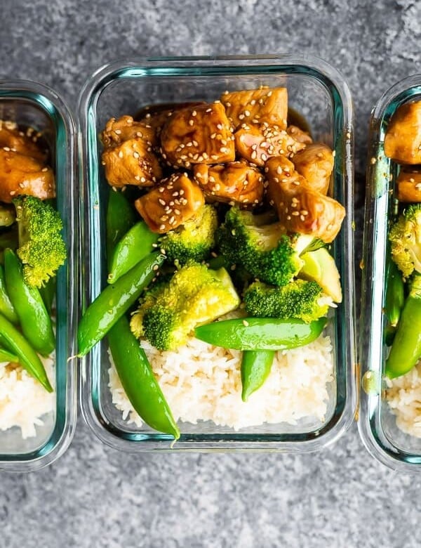 overhead shot of glass meal prep containers filled with honey sesame chicken lunch bowls